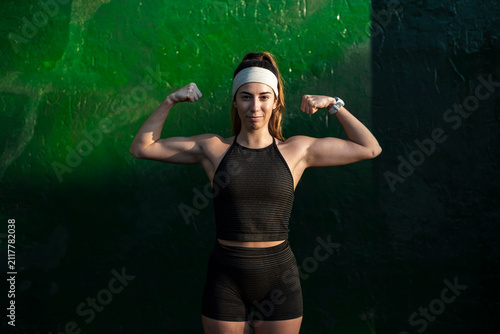  Strong woman flexing both biceps against a green wall