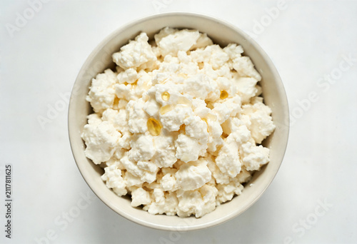 Fresh organic curd cottage cheese in a ceramic bowl on a white background