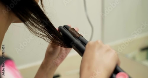 Young Asian woman styling hair using  a flat iron