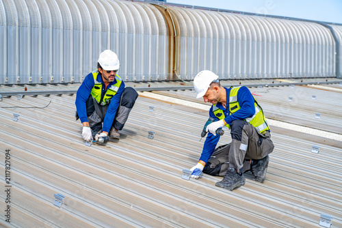 Workers install equipment on a roof during a sunny day