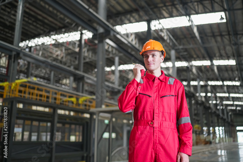 Worker in a red uniform wearing an orange helmet stands inside a large industrial warehouse during the day