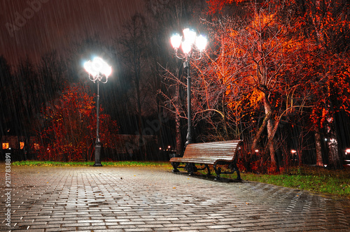 Fotografía Autumn night landscape of deserted park - a wooden lonely bench lit by street la