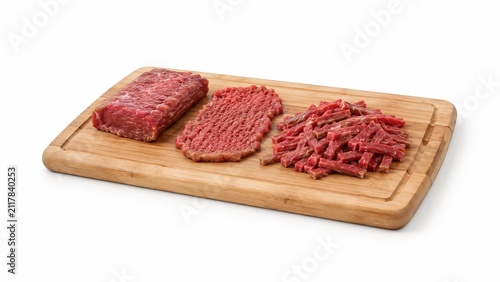 Raw beef assortment with whole piece, tenderized steak and sliced strips on a wooden cutting board isolated on white background