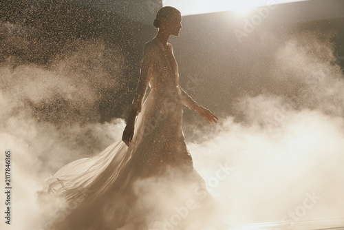 Elegant woman walking through glowing golden mist, artistic luxury fragrance concept with flowing fabric for premium beauty and fashion campaigns.