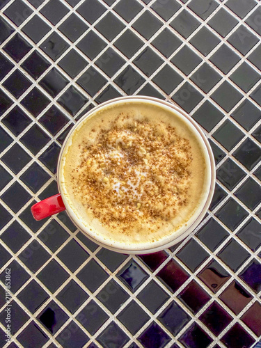 A warm cup of creamy latte topped with a dash of cinnamon, placed on a stylish tiled surface.