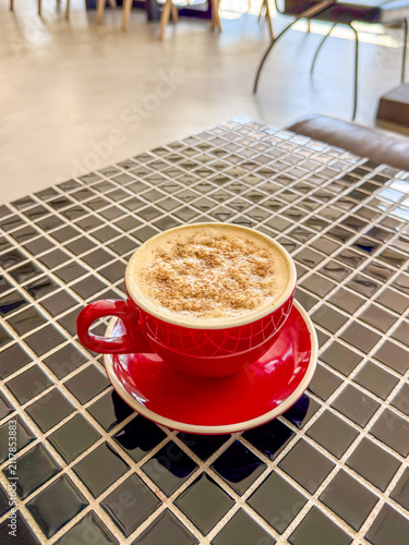 A vibrant red coffee cup filled with frothy cappuccino, resting on a glossy black tiled table.