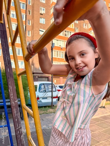 A cheerful young girl of Caucasian descent playing on a climbing frame in a vibrant urban playground.