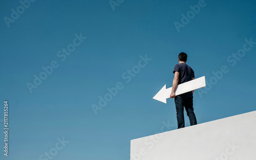 Business concept of making decisions with man holding left-pointing white arrow sign on high wall direction decision business navigation strategy pointing opportunity standing thinking