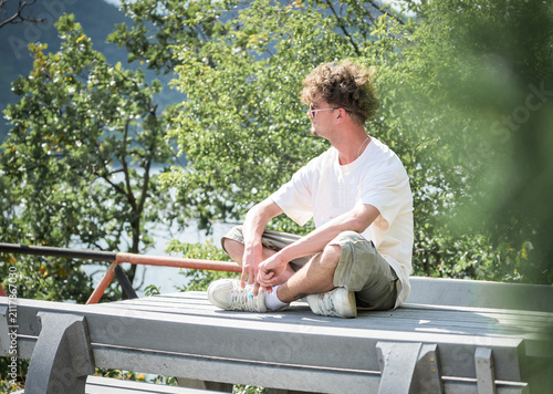 A handsome young man on vacation, sitting in a comfortable position and admiring the scenery. Casual, fashionable. Young man with glasses and curly hair.
