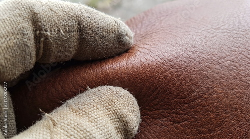 Close up of a worker hand in a protective fabric glove checking the texture and suppleness of brown leather