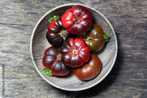 Fresh heirloom tomatoes in rustic wooden bowl on weathered wood table, top view