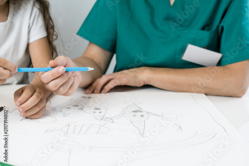 Konstfotografi A professional therapist in uniform holding a blue pencil to guide a left-handed young patient during a home healthcare session