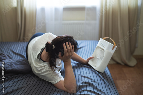 Woman suffering from heatwave using a portable fan