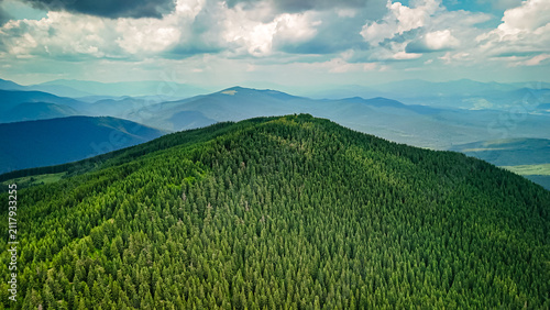 Cuadro en lienzo Drone view of a lush evergreen ridge rising above rolling forests while distant blue ranges fade under stormy clouds