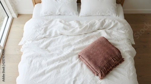 Top view of a cozy unmade double bed with white linen bedding and a decorative patterned throw pillow