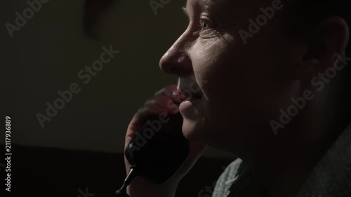 Woman talking on landline phone in dimly lit room in evening