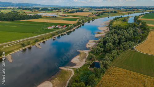 Ein Fluss fließt durch eine Landschaft mit Feldern und Bäumen in der Nähe von einer kleinen Siedlung