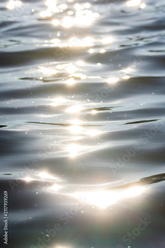 Sunlight sparkles dance across gentle ripple on a calm lake surface creating a dreamy pattern of silver highlights and soft waves An abstract nature background of shimmering reflections
