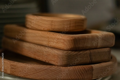 Wooden trays stacked on a table next to ceramic plates in a kitchen setting