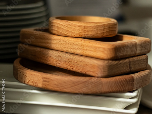 Wooden trays stacked on a table next to ceramic plates in a kitchen setting