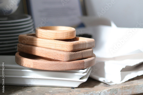 Wooden trays stacked on a table next to ceramic plates in a kitchen setting