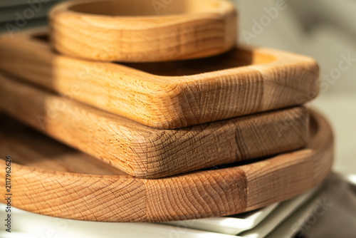 Wooden trays stacked on a table next to ceramic plates in a kitchen setting
