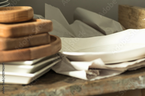 Wooden trays stacked on a table next to ceramic plates in a kitchen setting