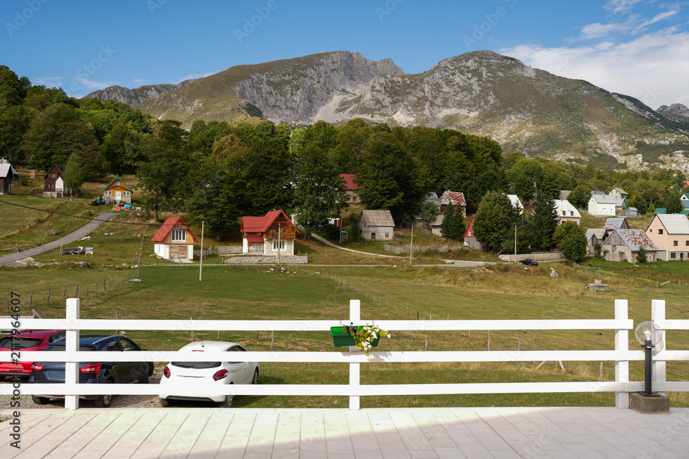 Fototapeta premium Scenic view of a mountain village with small houses, green slopes and rocky peaks in Durmitor, Montenegro