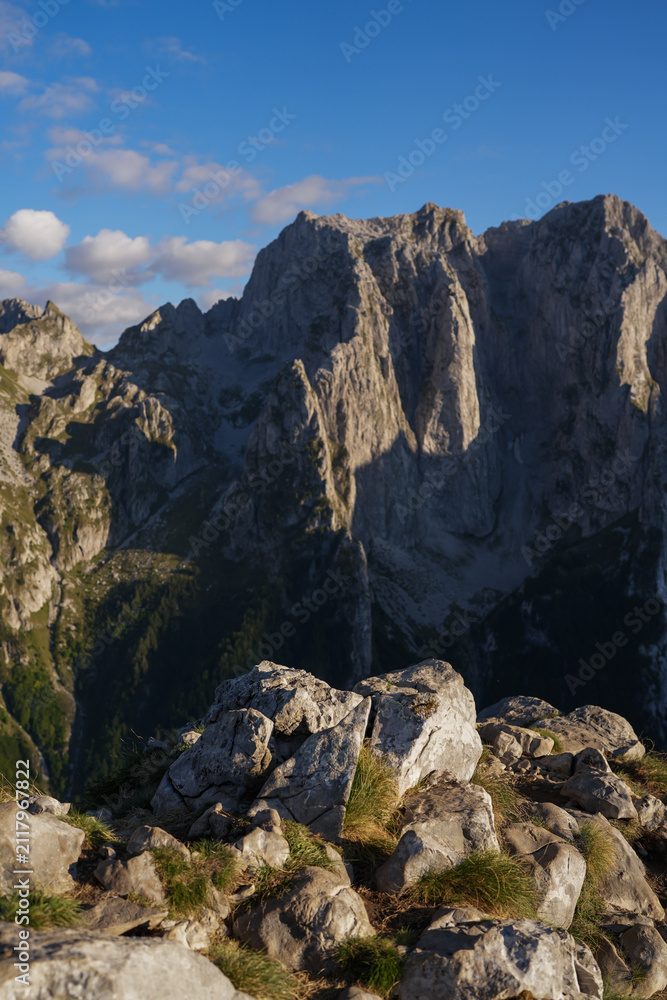Obraz premium Rocky mountain foreground with dramatic rugged peaks and blue sky in warm afternoon sunlight in Montenegro