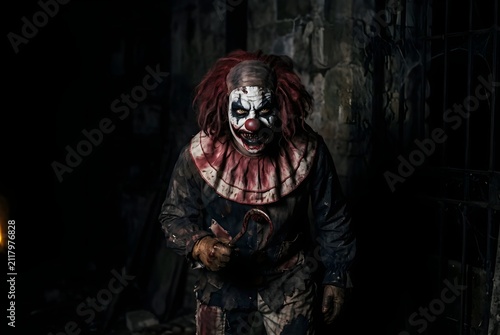 Scary evil clown standing inside a dark abandoned circus