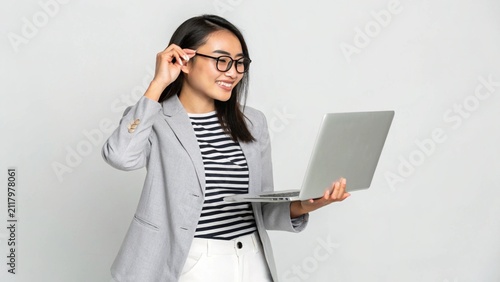 Smiling Young Asian Businesswoman Holding Laptop and Adjusting Glasses on White Background