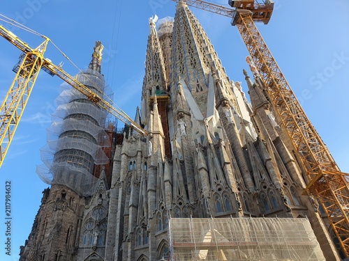 Konstfotografi Low angle view of the Sagrada Família basilica in Barcelona, Spain, showing multiple ornate stone spires with intricate Gothic and Art Nouveau architectural details against a clear blue sky