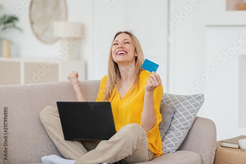 Foto Joyful Woman With Light Blonde Hair Enjoying Successful Online Shopping With Credit Card While Sitting On Couch At Home