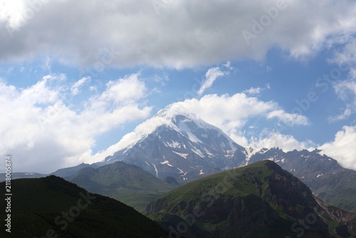 Snow covered summit of Mount Kazbegi emerging through clouds in Greater Caucasus range