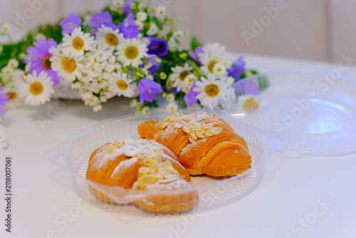 Golden croissants with delicate layers and a light dusting of powdered sugar are arranged among blooming daisies and bluebells. A bright, elegant bakery composition perfect for breakfast .
