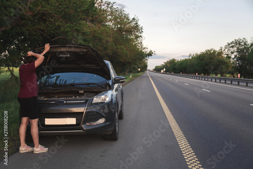 Frustrated woman standing beside broken car with open hood on roadside highway, facing unexpected vehicle breakdown during road trip, expressing transportation problem, travel emergency, 