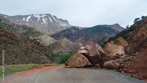 Fotografie Massive rockslide blocking mountain road with snow covered Atlas peaks in the ba