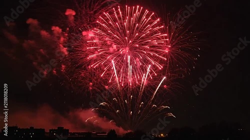 Bright colorful fireworks explode in the dark night sky above city