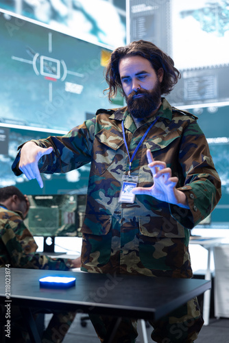 Obraz na płótnie A military officer enlarges a holographic battlefield on a command post table; the army strategist examines augmented reality enemy targets while preparing combat tactics for defense planning