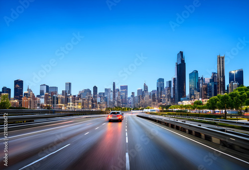 Car driving on a highway at dusk with a modern city skyline and illuminated buildings in the background, a car drives on a highway at dusk, with motion blur indicating speed and movement