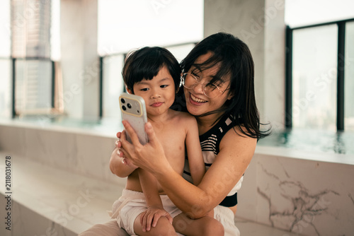 Mother and son taking selfie by modern swimming pool, happy family moments