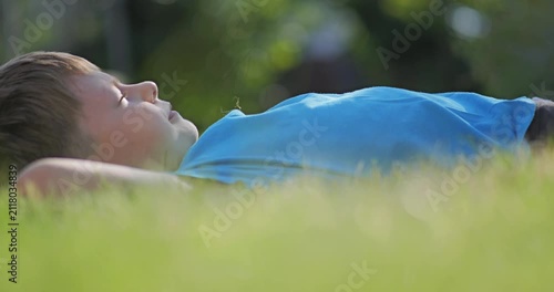 Little kid laid back on lawn grass, daydreaming with closed eyes outdoor in nature