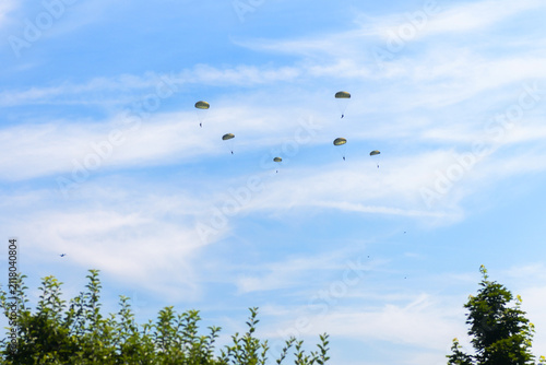 Fotografie Group of paratroopers descending with green parachutes against a blue sky