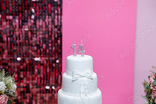 Elegant three tier white birthday cake with silver glitter fourteen candles in pink