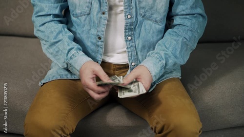 Close-up of a person counting a stack of US dollar banknotes while sitting on a sofa. Everyday money handling and personal finance concept focused on cash, savings, budgeting, income, finplanning.