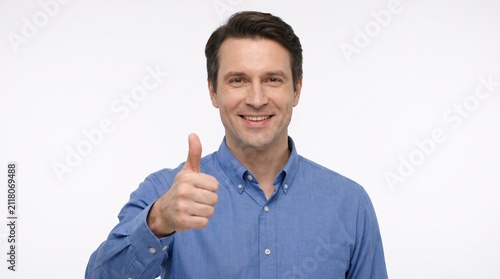 A smiling man giving a thumbs up gesture. He is wearing a blue collared shirt and has short brown hair
