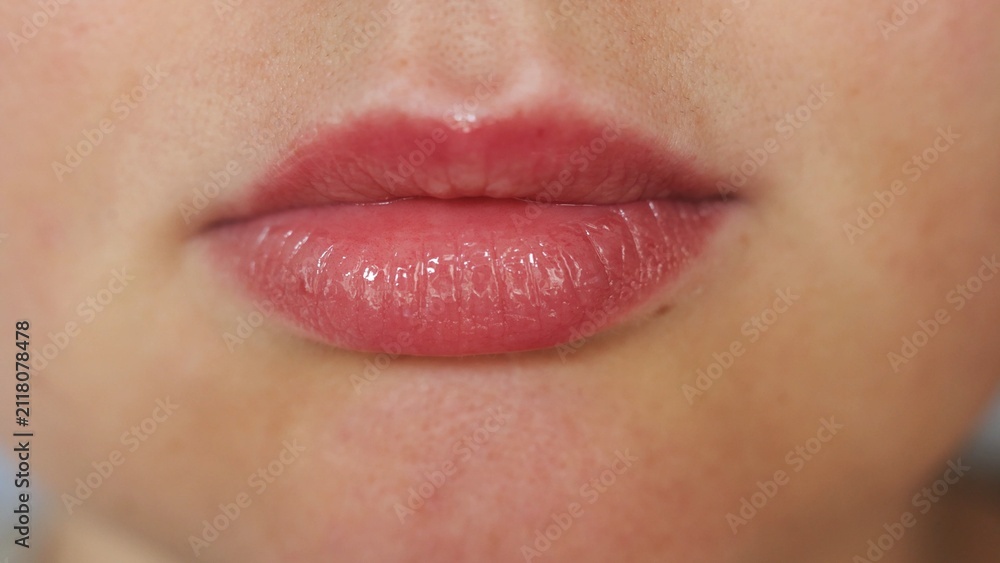 Obraz premium Close-up of a woman's full lips with glossy pink lipstick and subtle freckles