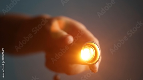 Close-up of a hand holding a small flashlight with a bright glowing light
