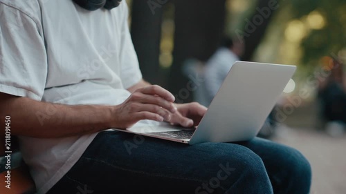 Man typing on laptop outdoors while seated wearing headphones