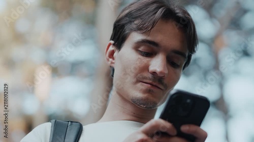 Close up of young man walking outdoors using smartphone with both hands looking at screen